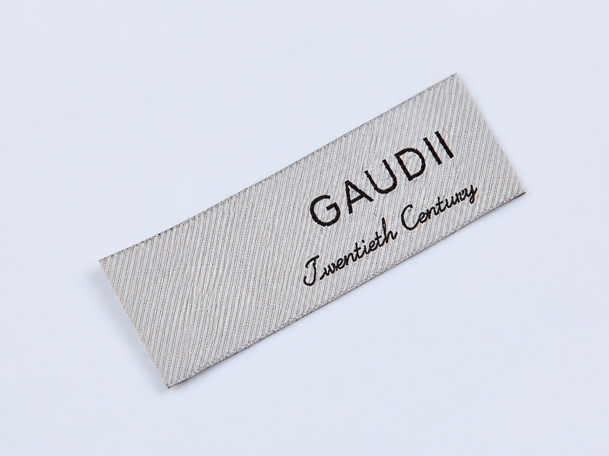 Ivory woven clothing label with black lettering and visible fabric texture, shown as a custom label example